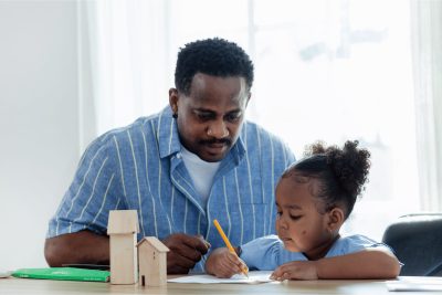 Father helping his young daughter draw at a table