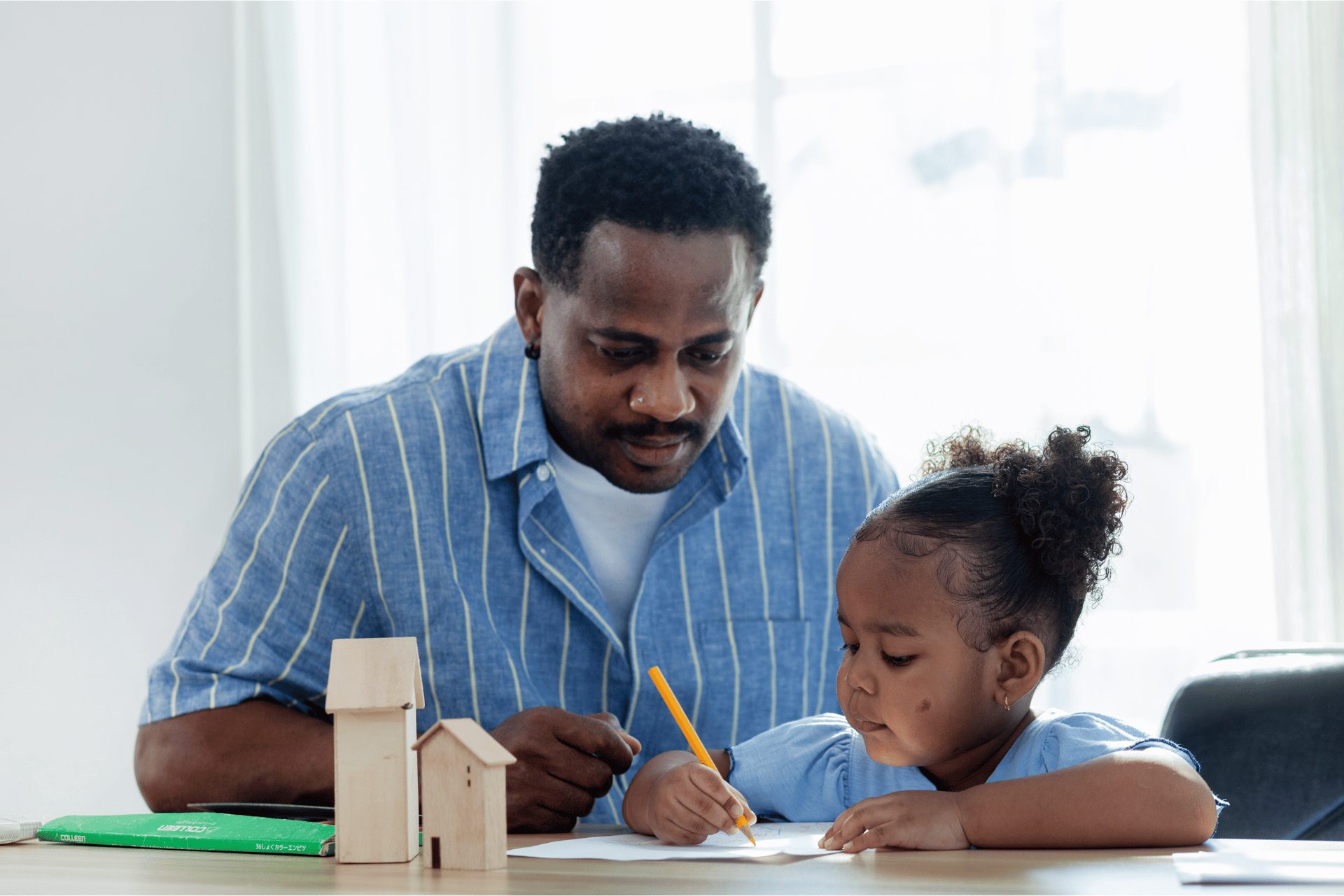 Father helping his young daughter draw at a table